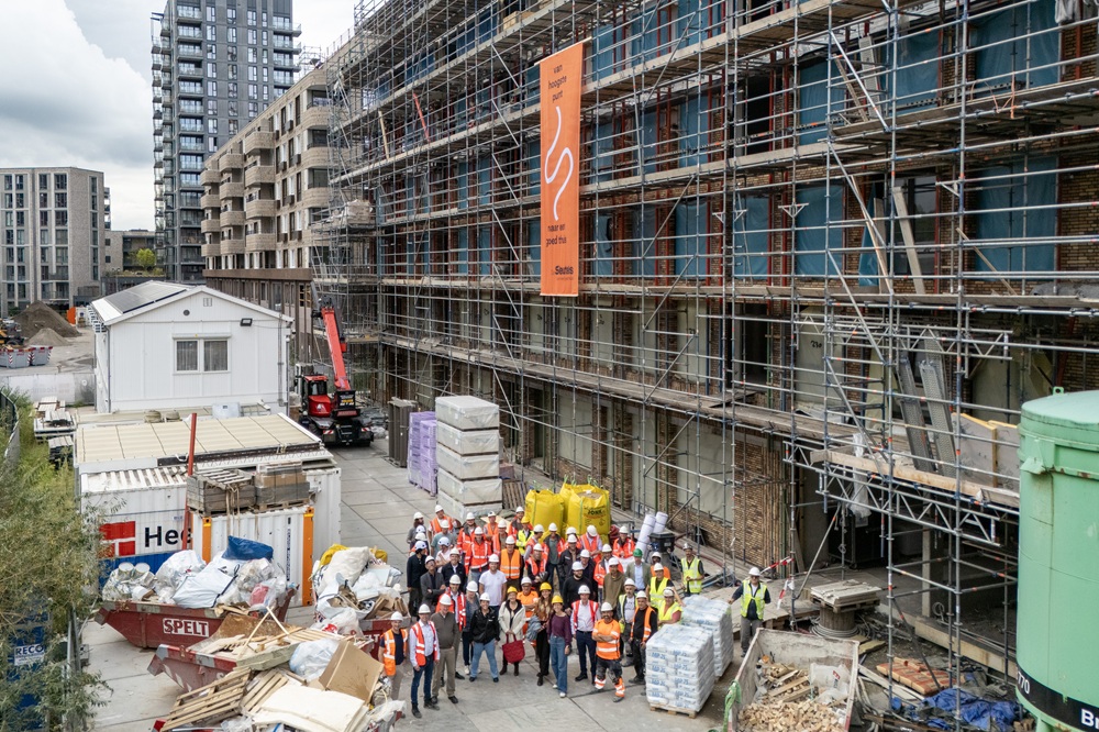 Groep mensen met helmen en hesjes op bouwplaats van Kappa en Omega