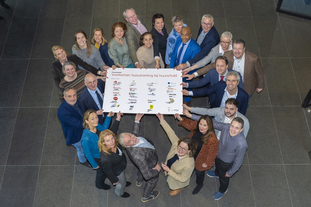 groep mensen die samenwerken op gebied van huurschuld en huisuitzetting. Zij houden een bord met handtekening vast.