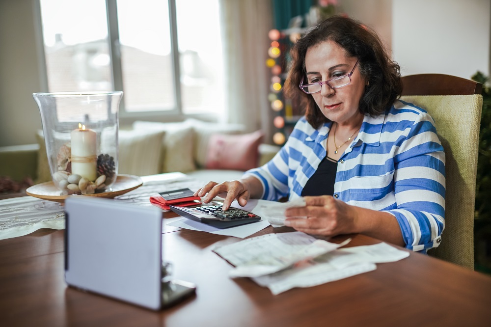 Mevrouw aan tafel met rekenmachine en laptop en papieren rekeningen