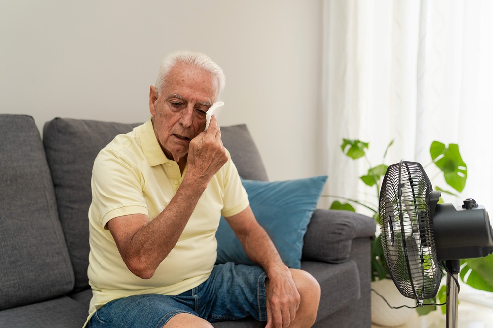 oudere man dept zijn gezicht zittend op de bank met ventilator op zich gericht