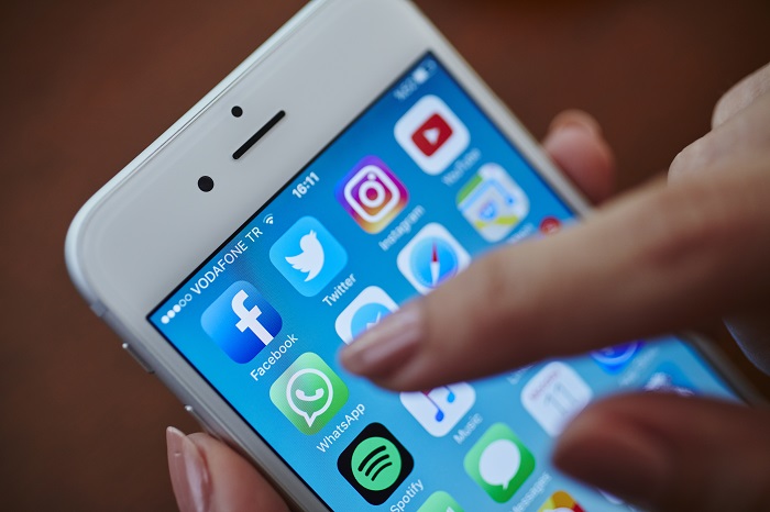 Iphone met appjes op scherm en vinger die op icoon whatsapp drukt