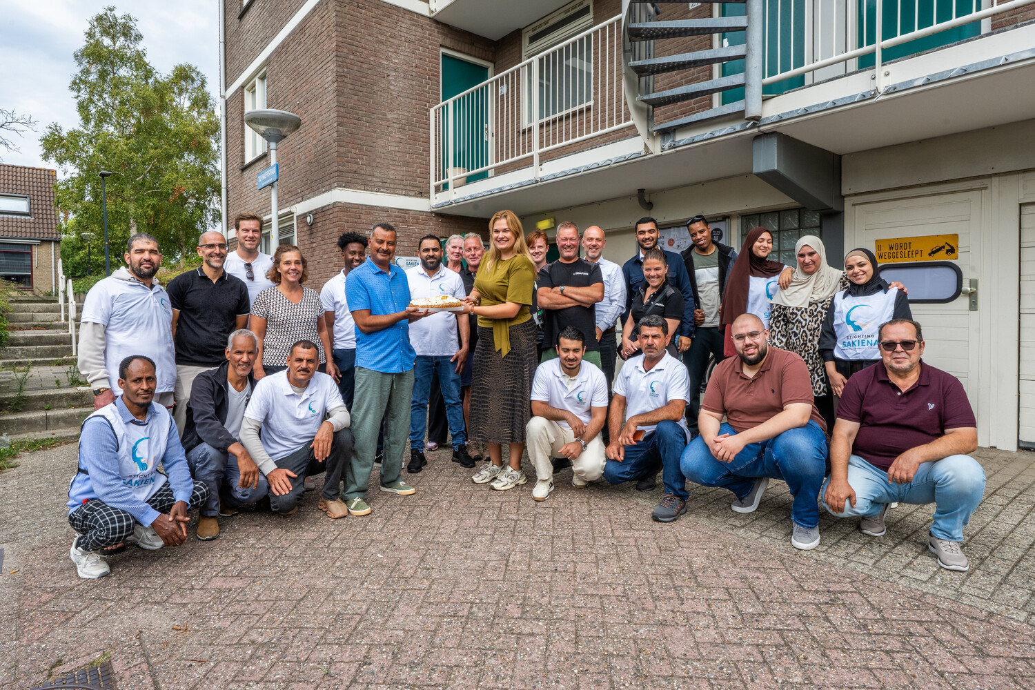 De teams van De Sleutels en Stichting Sakiena poseren met taart om hun samenwerking te vieren