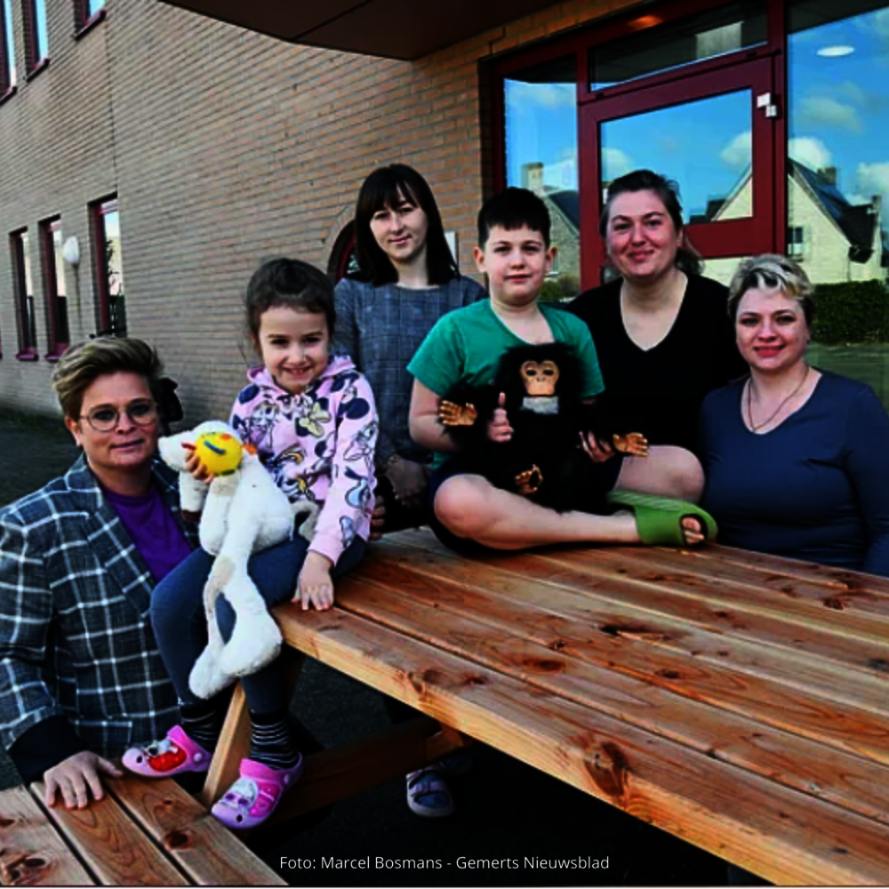 Dorpsondersteuner Linda met de geïnterviewde Oekraïense dames en twee van hun kinderen op de picknicktafel bij hun opvanglocatie.