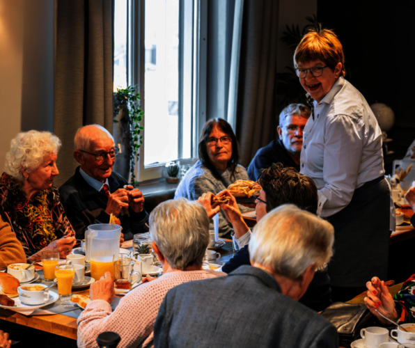 Tafel met eten en drinken met daaromheen een aantal huurders en iemand van de bediening die lacht