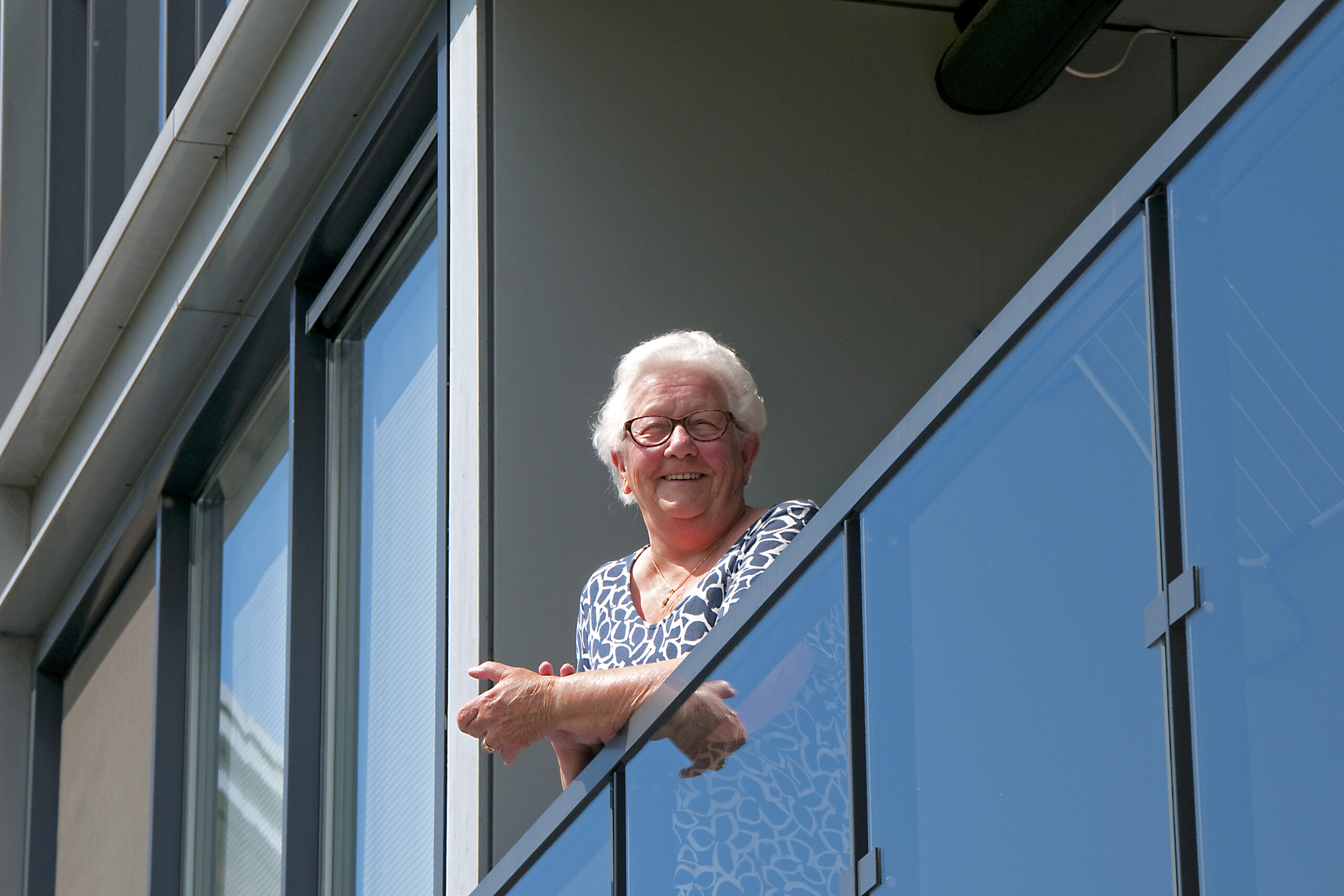 Foto van huurder Mien die lachend op de rand van haar balkon hangt.