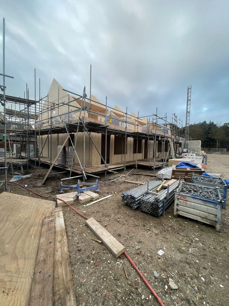 Foto van een rijtje houtbouw woningen in aanbouw met steigers en de eerste houten wanden die rechtop staan.