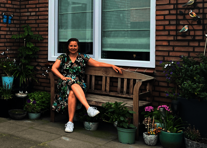 Wiesje op haar tuinbank in de achtertuin omringt door bloemen en potten.