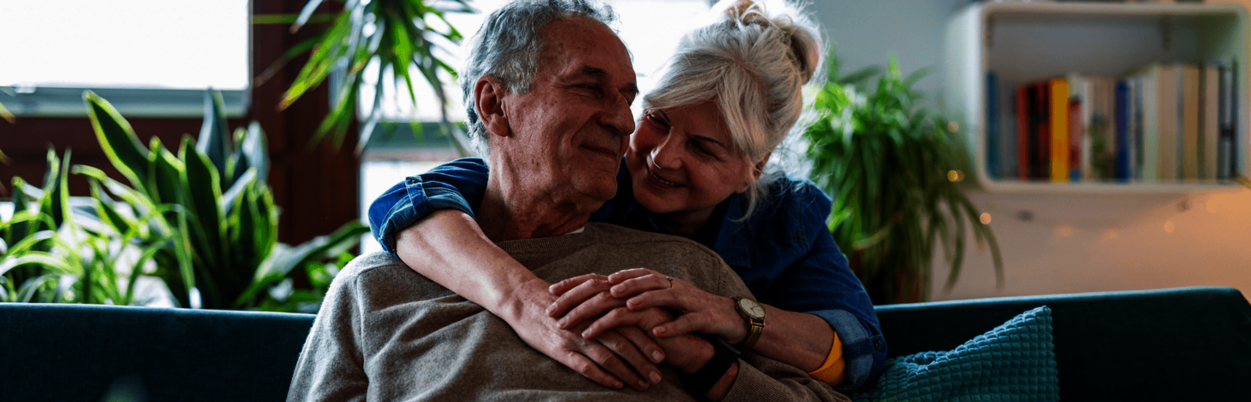 Foto van een lachend en knuffelend senior stel op een bank in hun woonkamer.