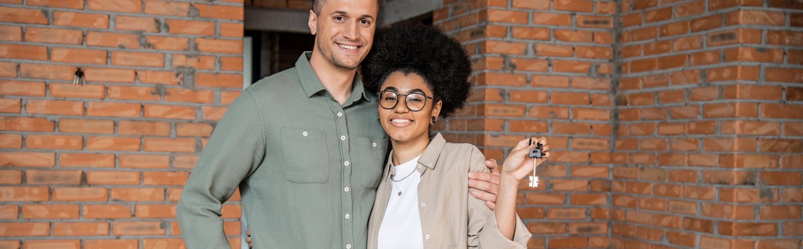 Jong stel met sleutel van hun nieuwe woning voor hun deur met stenen gevel.
