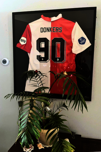 Ingelijst Feyenoord shirt van Henk met de naam Donkers achterop. Hangend boven een kastje met een plant.
