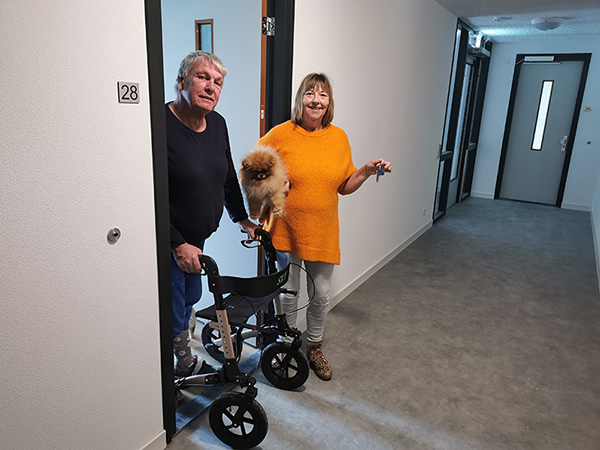 Ada en Peel in de deuropening van hun appartement. Peel met zijn rollator in de hand. Ada met de sleutel van hun nieuwe huis in de hand.