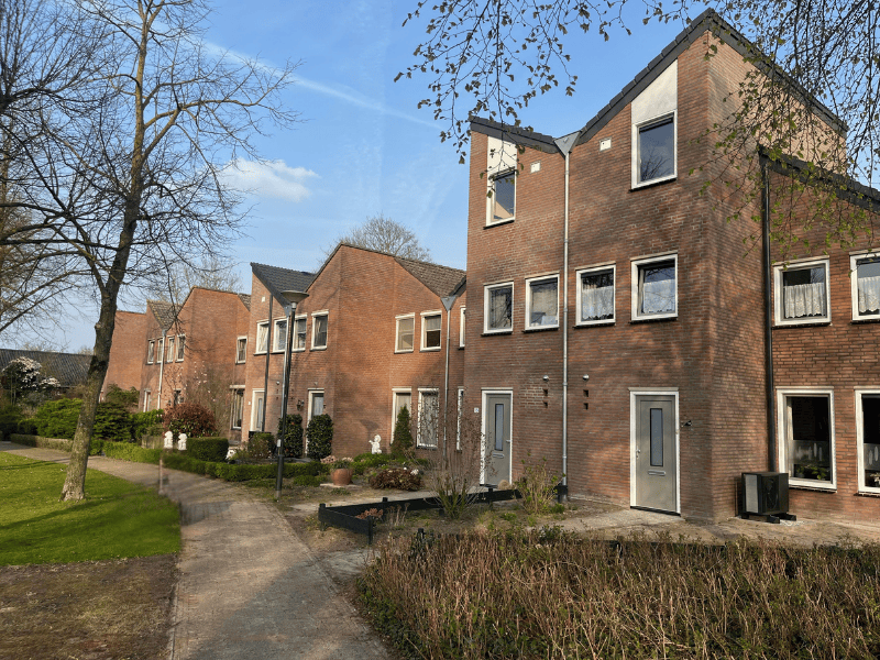 Foto van een rijtje gerenoveerde woningen aan een groen hofje in de zon