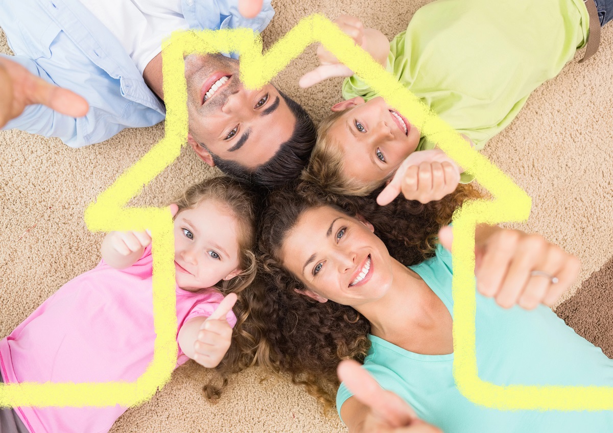 Foto van een gezin met 2 kinderen liggend op de grond met de duimen omhoog en hoofden bij elkaar. Daaroverheen staat een gele lijntekening van een huis.