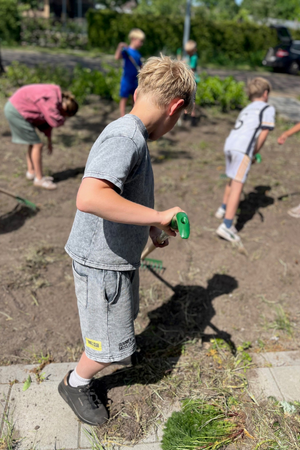 Foto van enkele kinderen aan het schoefelen en onkruid plukken in de tuinen.