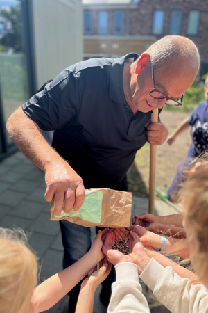 Jan Melis schud bloemzaadjes uit een zak in de handen van enkele kinderen.