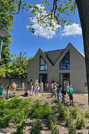 Foto van de twee woningen aan de Abtshof met een blauwe lucht en de kinderen aan het werk in de voortuinen.