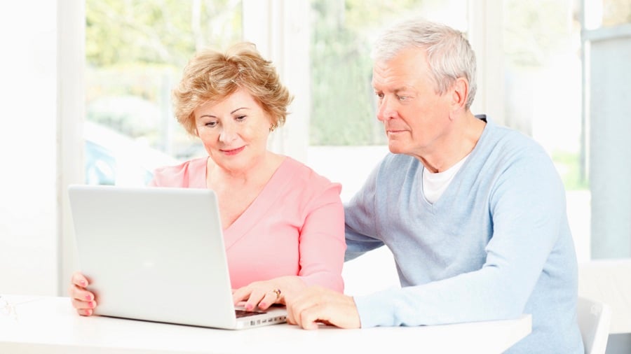 Ouder stel zittend aan tafel achter een laptop.