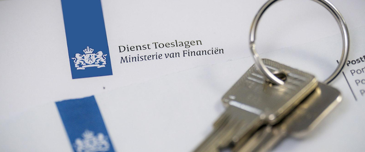 Stukje van een envelop van overheid met blauwe logo en tekst Dienst Toeslagen. Op de envelop ligt een ring met 2 huissleutels.