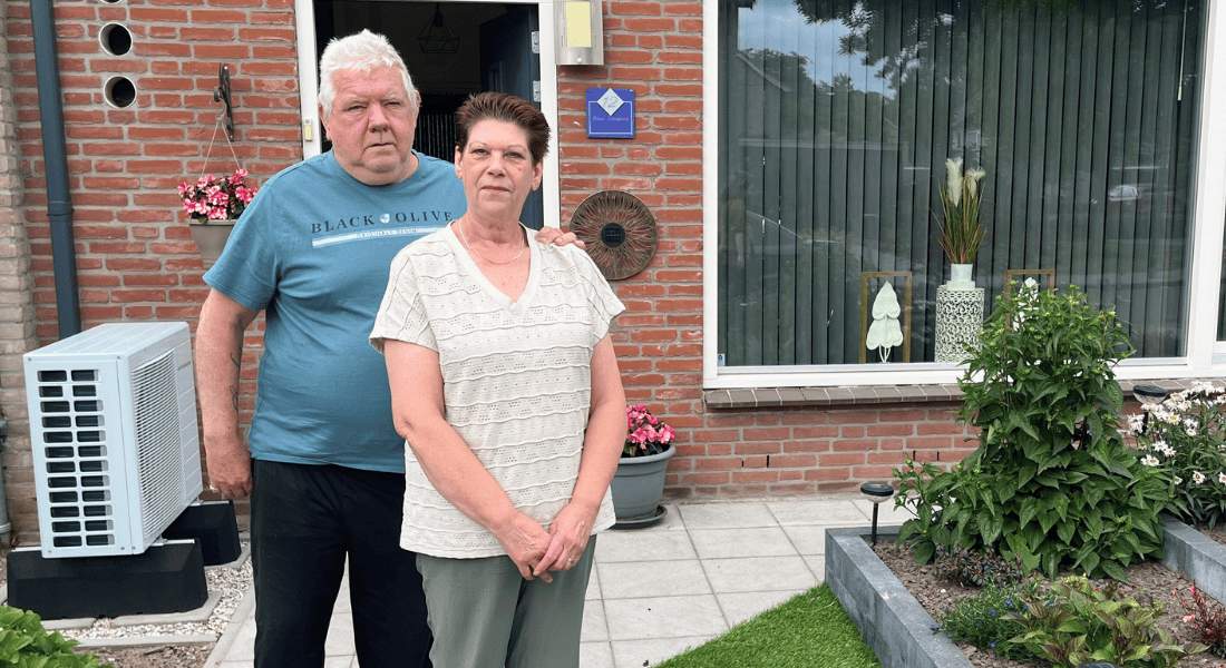 Eri en Gerard in de voortuin van hun woning met op de achtergrond de buitenunit van de hybride warmtepomp naast hun voordeur.