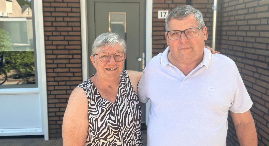 Jan en Francie in de zon voor hun gerenoveerde woning. Vanaf hun middel tot hoofd op de foto. Jan met witte polo. Francie met een zwart/witte mouwlos hes. Beiden dragen een bril.