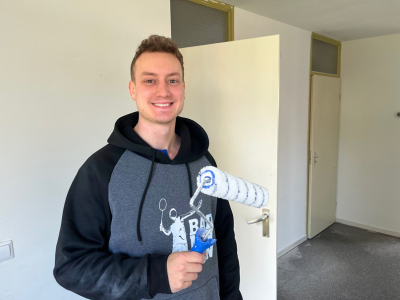 Kristof staand in zijn woning. Glimlachend. Met een verfroller in zijn hand met witte verf.