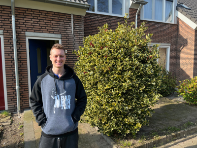 Kristof staand voor zijn woning aan de voorkant. Met voor de woning een hele grote groene struik.