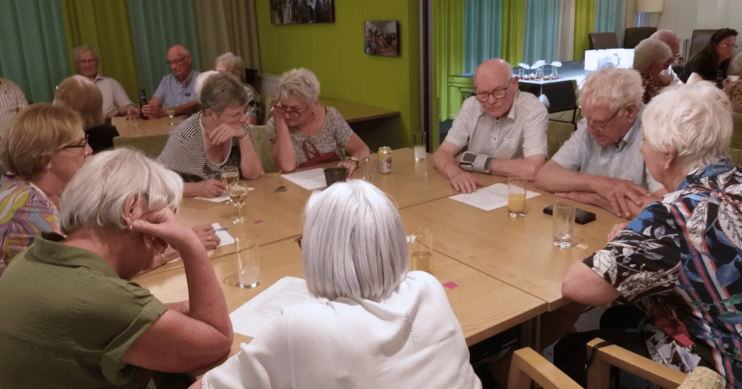 Groep oudere huurders om een grote tafel bezig met een quiz. Op de achtergrond nog een groep.