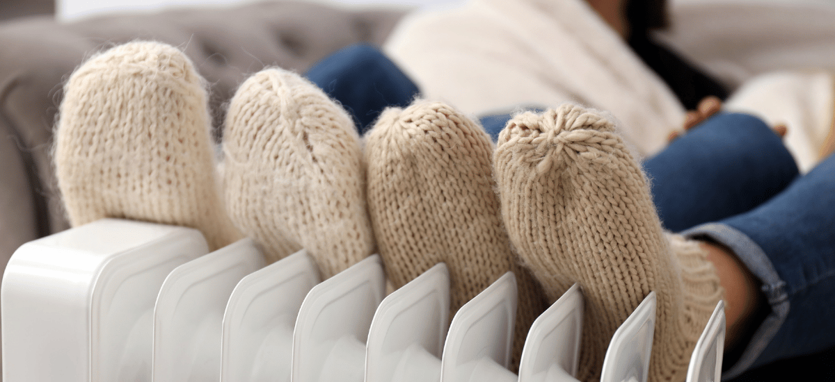 Twe paar voeten in dikke beige sokken tegen een verwarming.