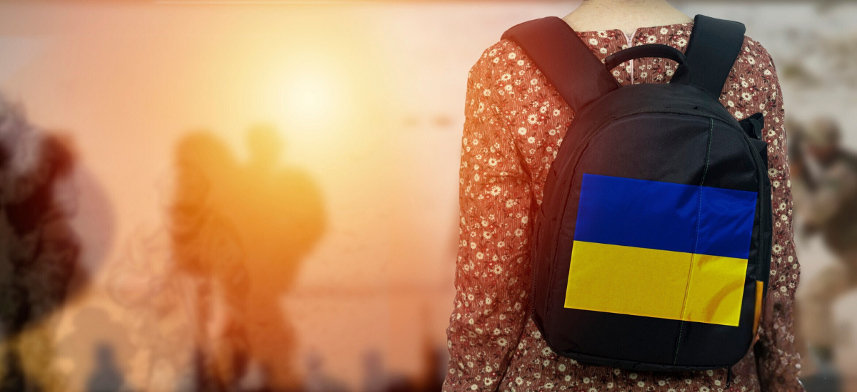 Rug van een vrouw met een rugzak met de vlag van Oekraïne tegen zonnige achtergrond met andere mensen in de verte.