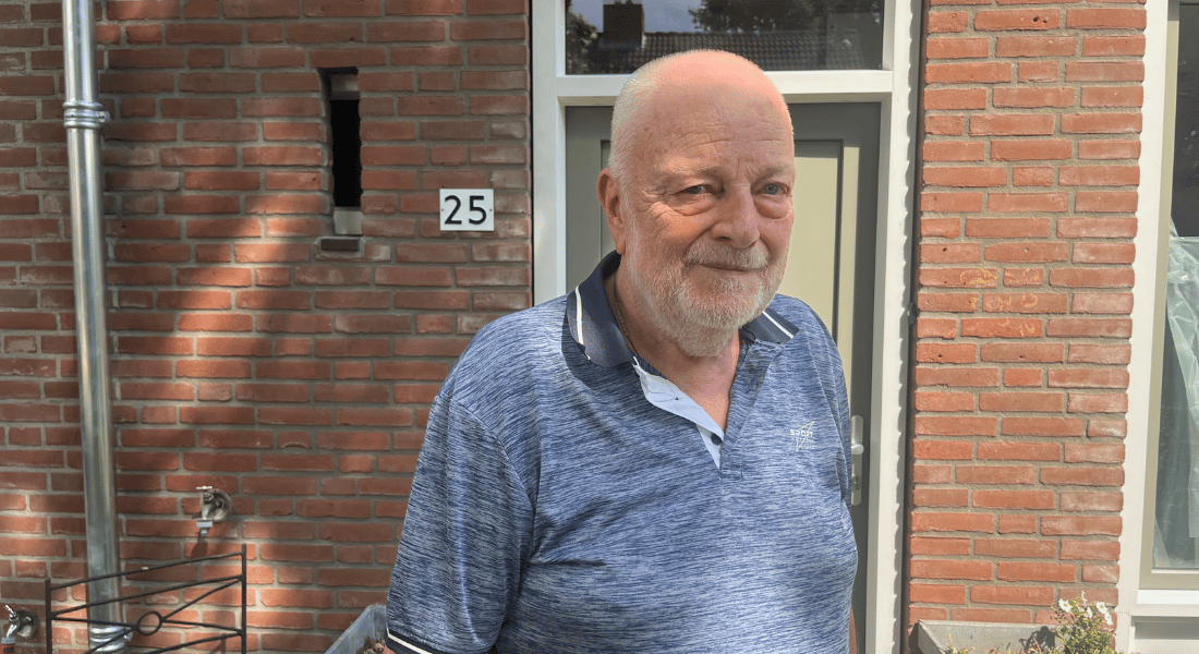Piet voor zijn woning (vanaf borsthoogte). blauwe polo. Zon schijnt door de bladeren van de bomen en je ziet de schaduwen van de blaadjes op de muur en op Piet.