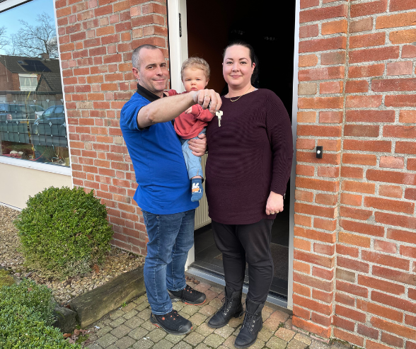 Het gezin voor de open voordeur van hun woning. Pim showt de huissleutel.