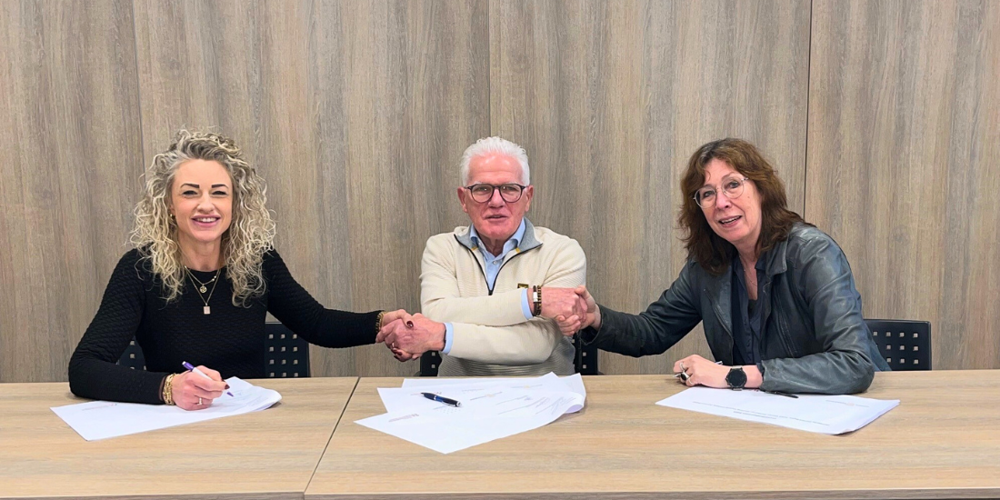 Foto van van de drie tekenende partijen aan tafel. Ze geven elkaar een hand.