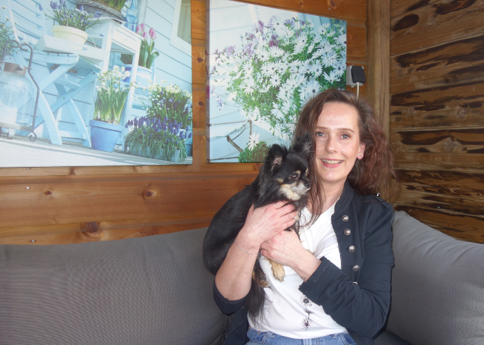 Huurder Saskia Dijkhof met haar hondje in de arm op een bank onder de overkapping in de achtertuin