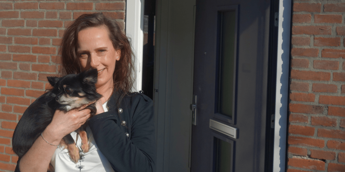 Saskia Dijkhof met haar hondje op de arm voor de geopende deur van haar woning