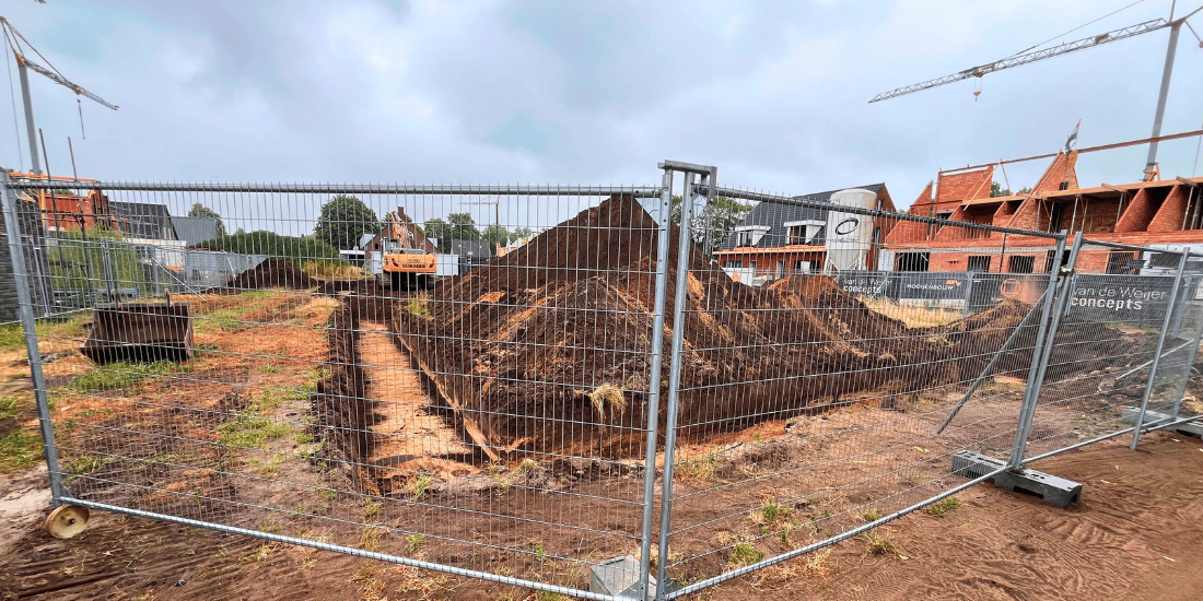 Foto van de bouwplaats met op de voorgrond bouwhekken en daarachter een bouwplaats van zand met eerste graafwerkzaamheden.