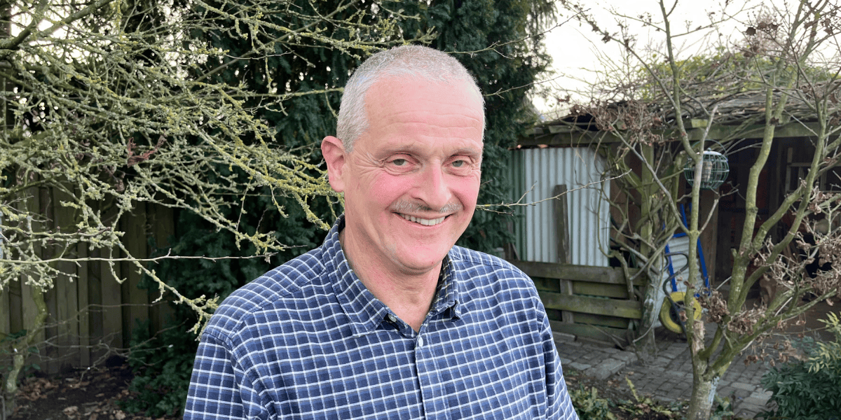 Tom van Woerden vanaf borsthoogte staande in een achtertuin. Lachend. Foto vanaf borsthoogte