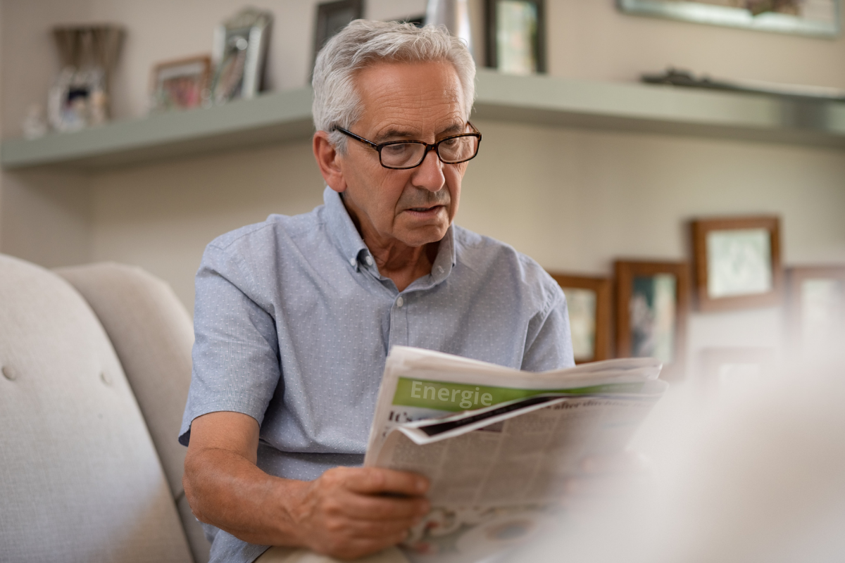 Oudere man zit op de bank en leest de krant