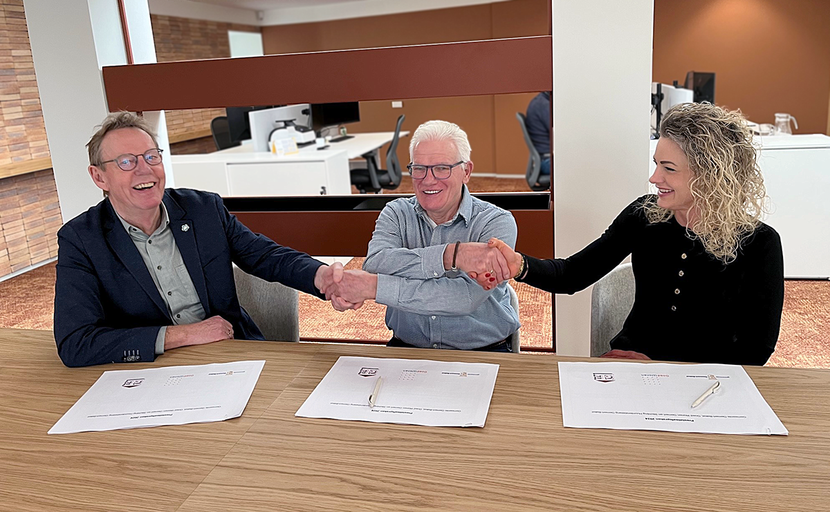 Hans, Gerard en Hanneke zitten met de getekende papieren aan tafel en schudden elkaar de hand.