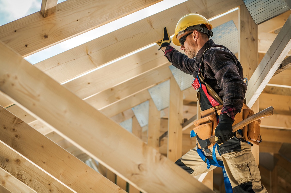 Foto van een man met werkkleding en helm in de nog van een houtbouw woning