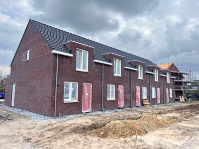 Foto van het rijtje woningen in aanbouw, schuin van links gefotografeerd. Buitenzijde helemaal gereed met kozijnen, ramen en deuren.
