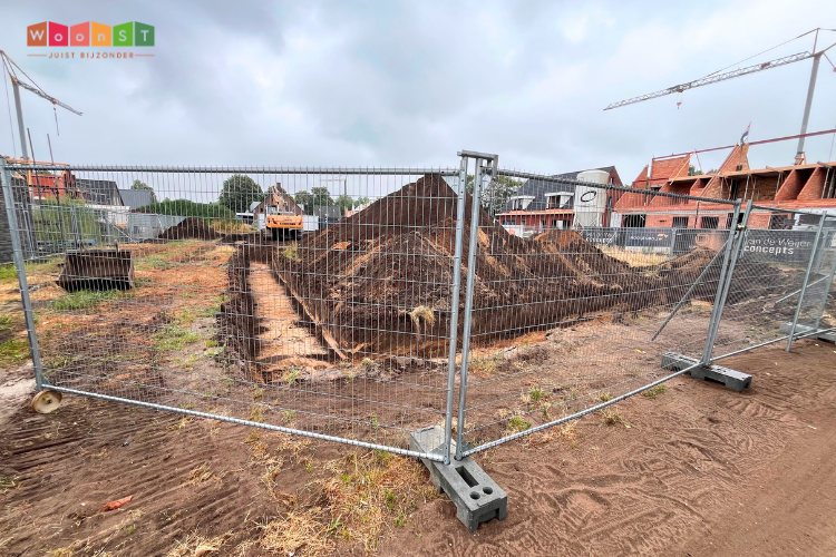 Foto van de bouwplaats met op de voorgrond bouwhekken en daarachter een bouwplaats van zand met eerste graafwerkzaamheden.
