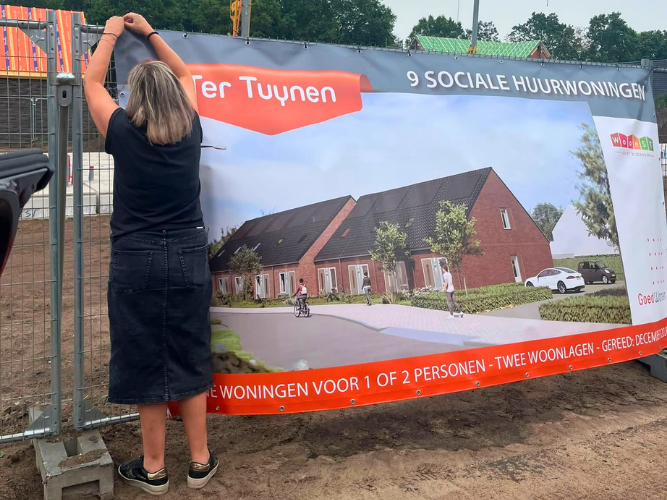 Wooncoach Mascha hangt een bouwdoek met een illustratie van de woningen op een van de bouwhekken.