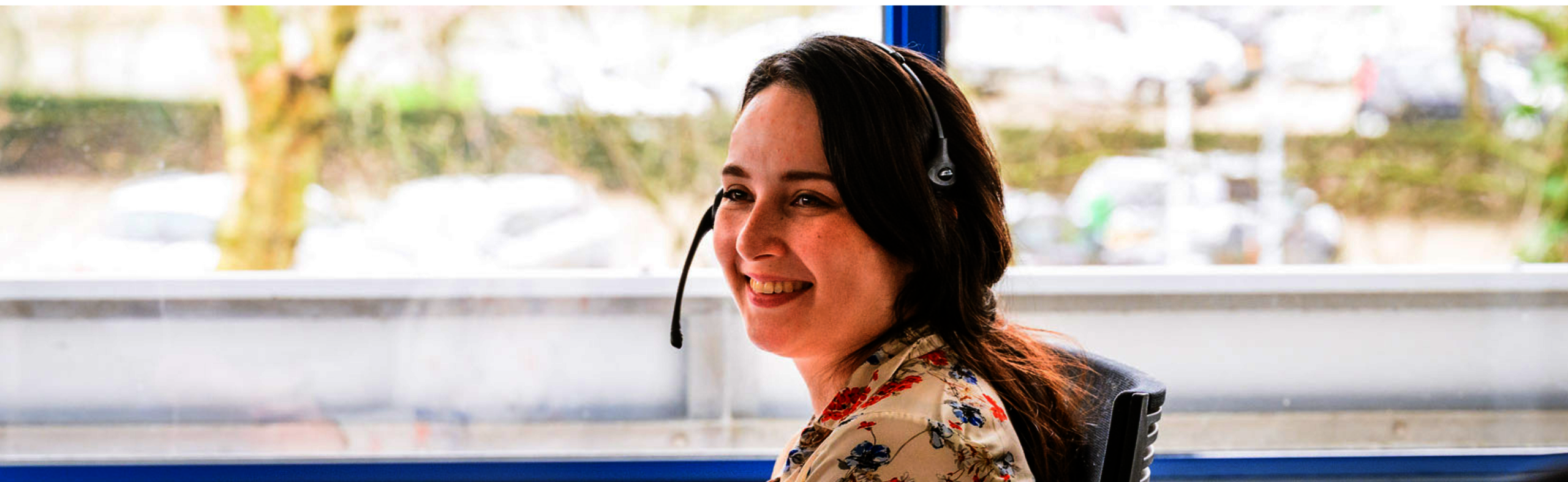 Foto van een lachende medewerker van het klant contact met een koptelefoon op.