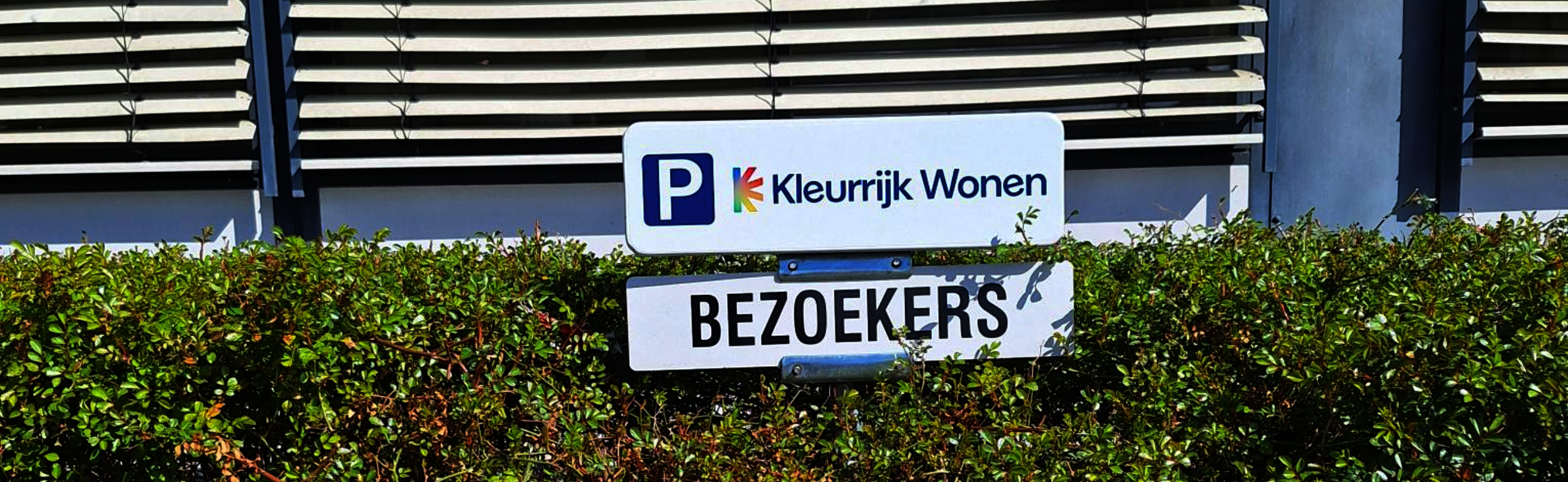 bordjes bij een parkeerplaats met de tekst "Kleurrijk Wonen" en "bezoekers"