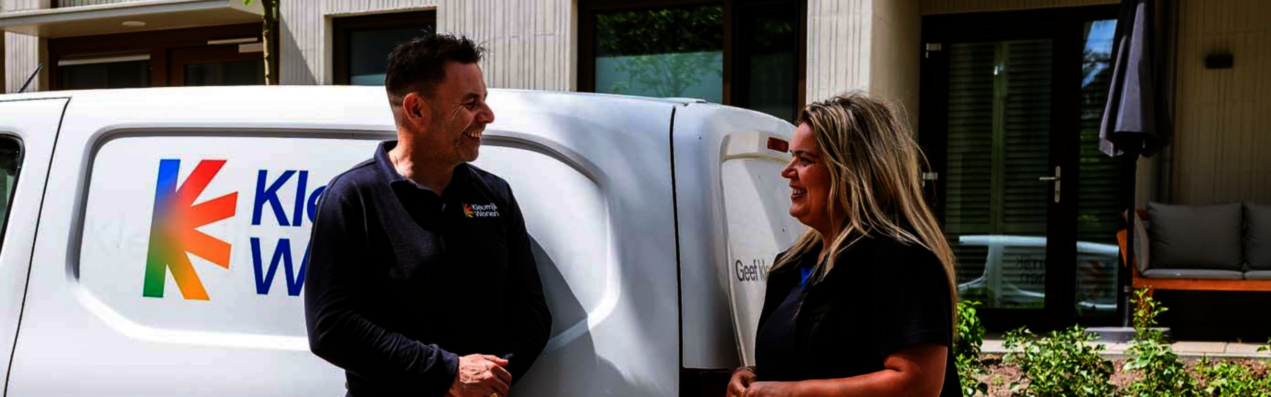 Twee wijkbeheerders staan naast een auto met het logo van Kleurrijk Wonen. 