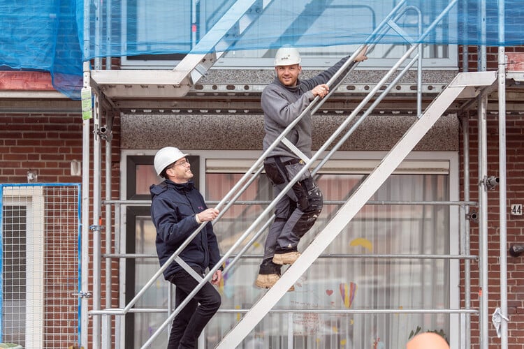 Bouwvakkers met helm op gaan de steiger bij een woning op