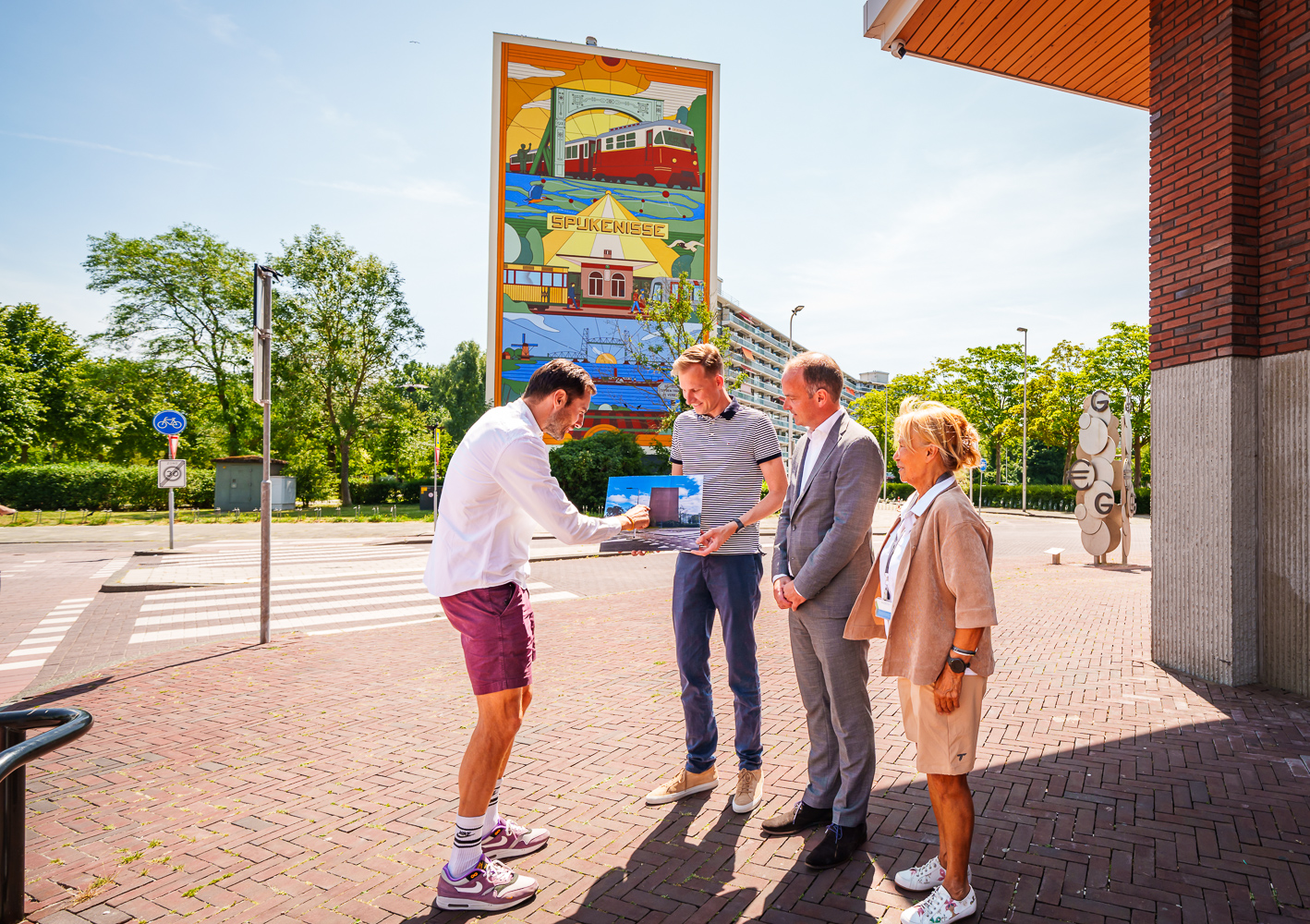 Foto-ok Wethouder Postma, kunstenaar Michiel Meulemans en bestuurder Ruud van Nieuwaal staan voor de mooi beschilderde kopgevel van de Marrewijkflat