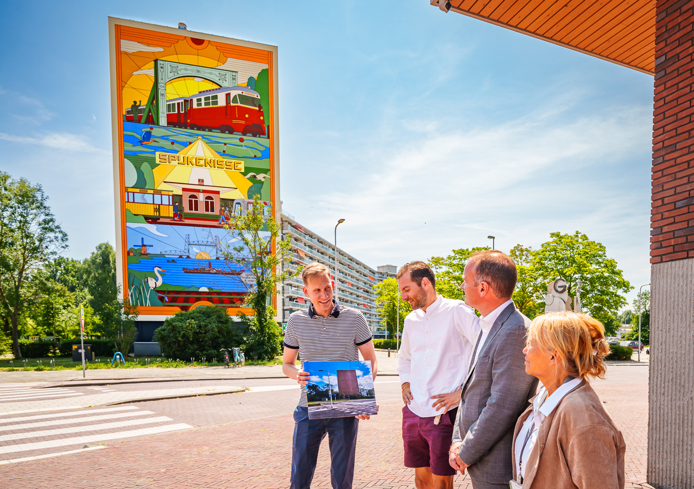 Foto-ok Wethouder Postma, kunstenaar Michiel Meulemans en bestuurder Ruud van Nieuwaal staan voor de mooi beschilderde kopgevel van de Marrewijkflat