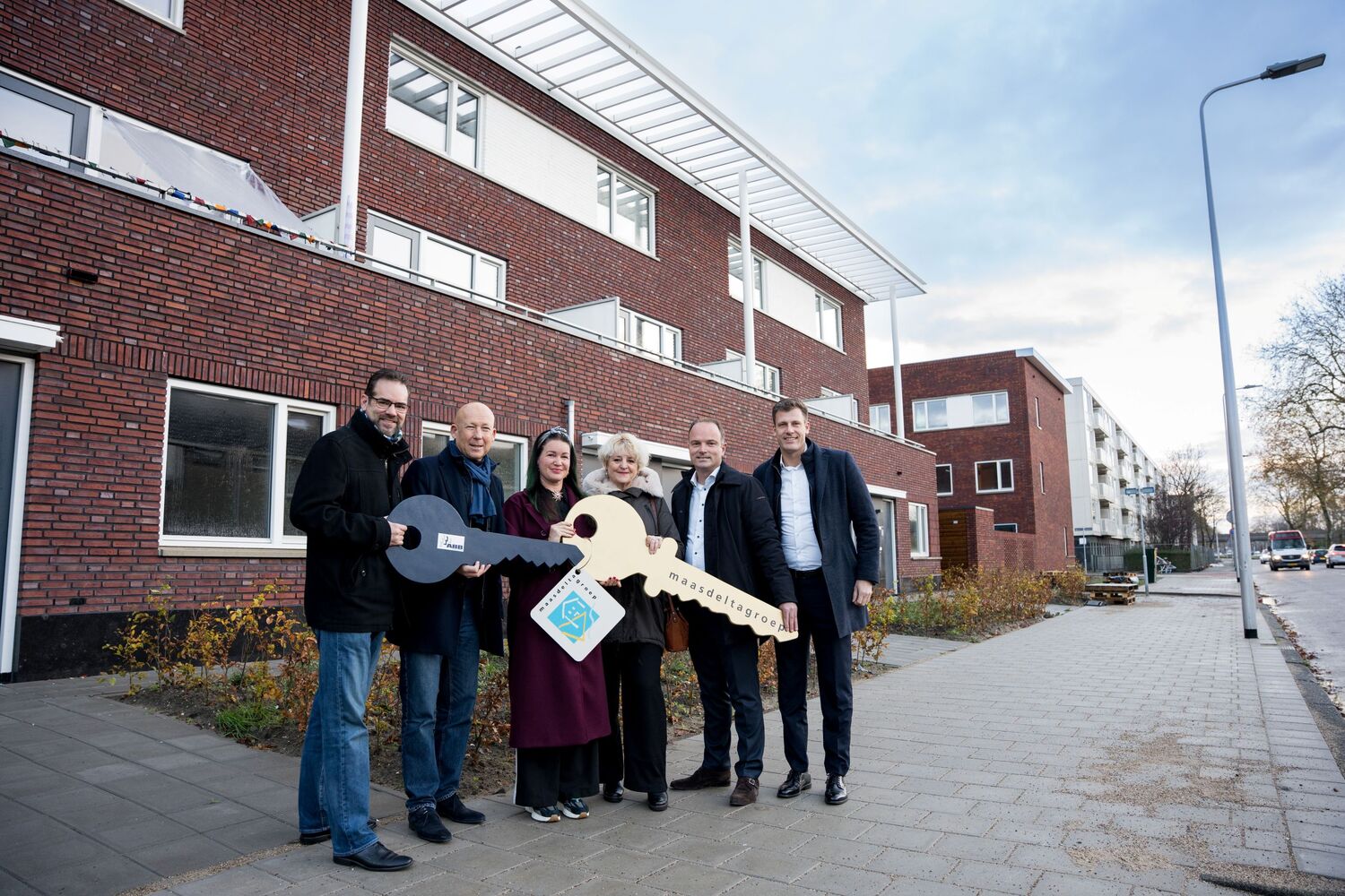 voor de nieuwbouw van links naar rechts wethouder Chris Hottentot, wethouder Mijnans, nieuwe bewoner, woonconsulent Marlies Bakelaar, bestuurder Maasdelta Groep Ruud van Nieuwaal en projectleider ABB Tim Schregardus