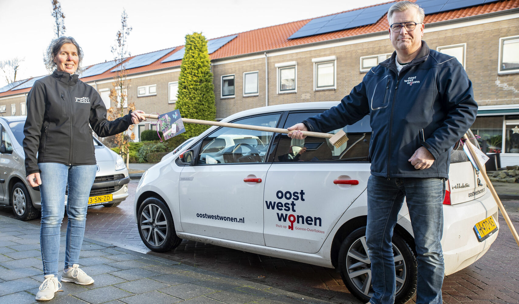 Een beeld van een huurder die een onkruidbezem ontvangt van opzichter Arnold van’t Wout van Oost West Wonen.